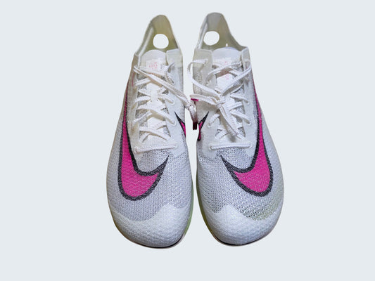 Białe kolce lekkoatletyczne Nike Air Zoom Victory z różowym logo marki od Latające Wieszaki na drewnianym podłożu.