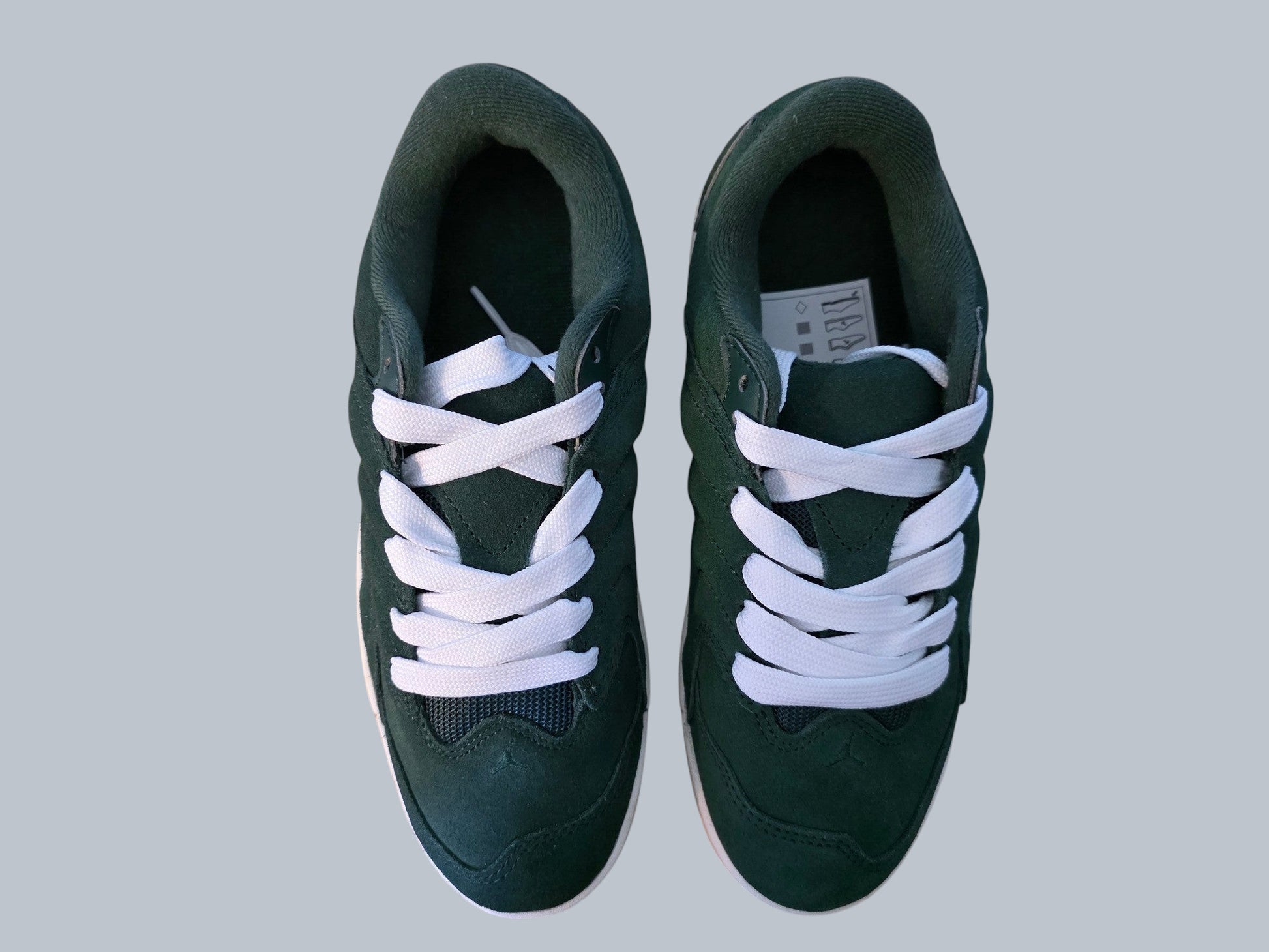 Męskie sneakersy Jordan Latające Wieszaki z zielonego zamszu z białymi sznurowadłami, widok z góry na drewnianym tle.