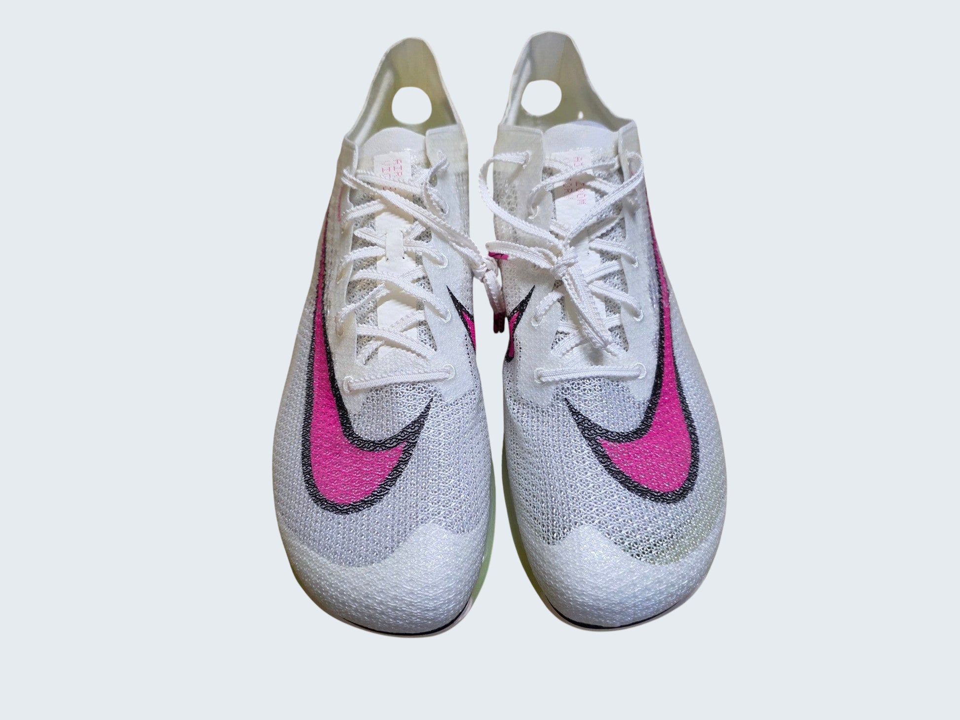 Białe kolce lekkoatletyczne Nike Air Zoom Victory z różowym logo marki od Latające Wieszaki na drewnianym podłożu.